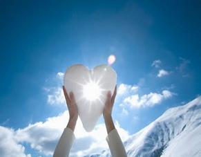 Hands holding snow shaped heart with burst of sunlight